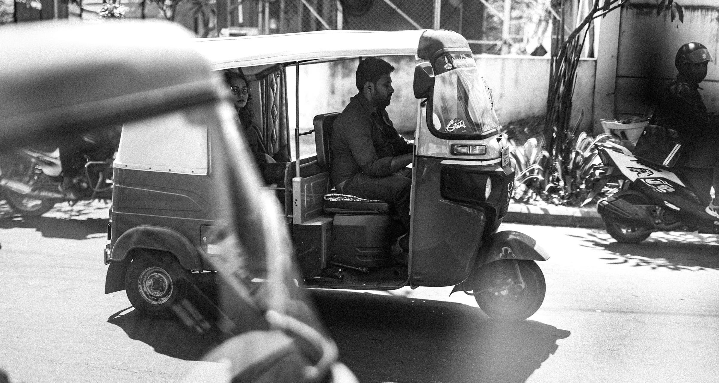 Three-wheeler in motion on an urban street, shown in black and white